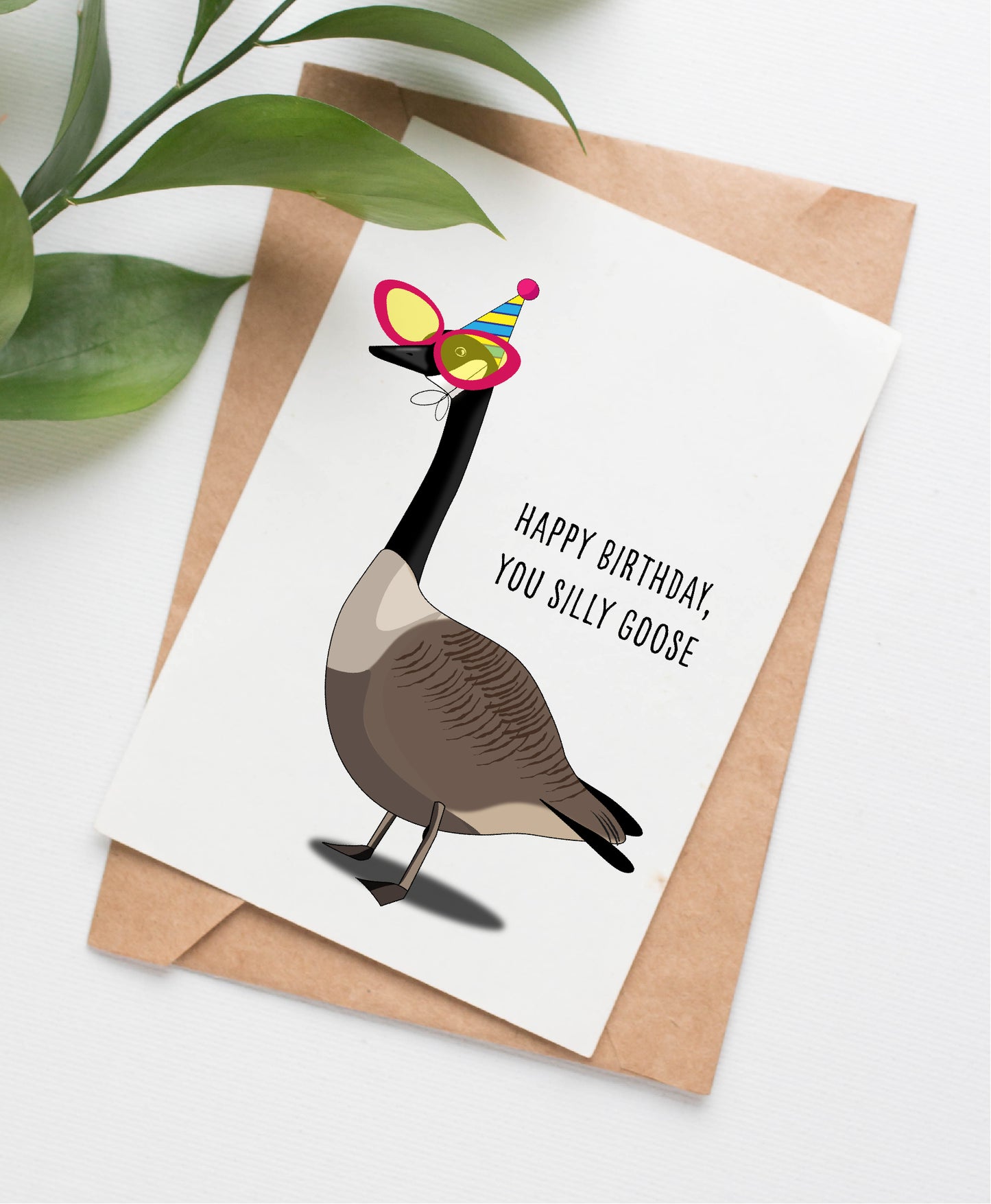 Picture shows greeting card with Canada goose illustration in vertical orientation. Goose is wearing oversized novelty sunglasses and a birthday party hat. Caption on card reads "HAPPY BIRTHDAY, YOU SILLY GOOSE." Card is pictured with a kraft brown paper envelope.