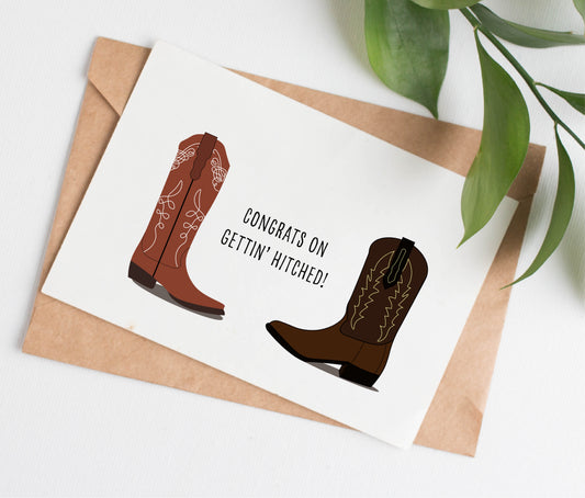 This cowboy boots wedding card is handmade in Canada. It shows two cowboy boots facing each other, one tall and light brown, the other shorter and dark brown. The text between them says "Congrats on gettin' hitched!"