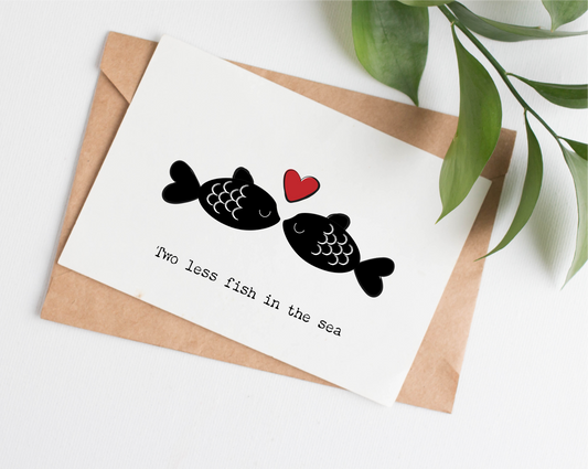 This wedding card is handmade in Canada. This card shows an illustration of two black fish with white outlined details. A red heart is between them. The text says "Two less fish in the sea"