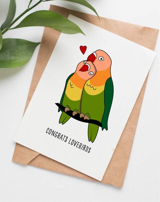 This handmade card is made in Canada. It shows two lovebirds snuggled up together with a red heart to the side. The text says "Congrats Lovebirds"