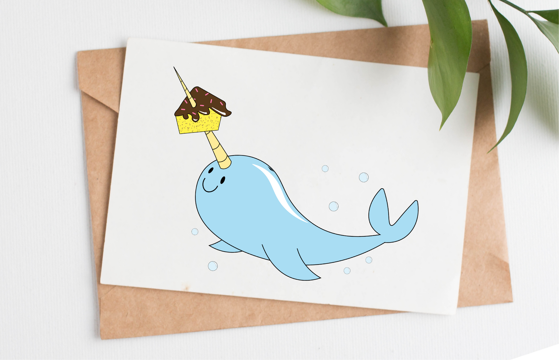 This handmade card is made in Canada. It shows a smiling narwhal with a big birthday cake slice speared on its tusk and bubbles all around.