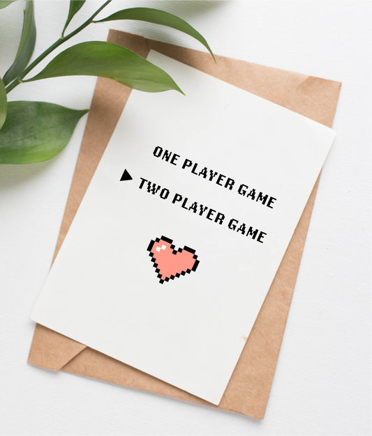 This wedding card is handmade in Canada. It shows an 8-bit style pixelated pink heart, with pixelated text above saying "One Player Game" and "Two Player Game." The Two Player option is selected.